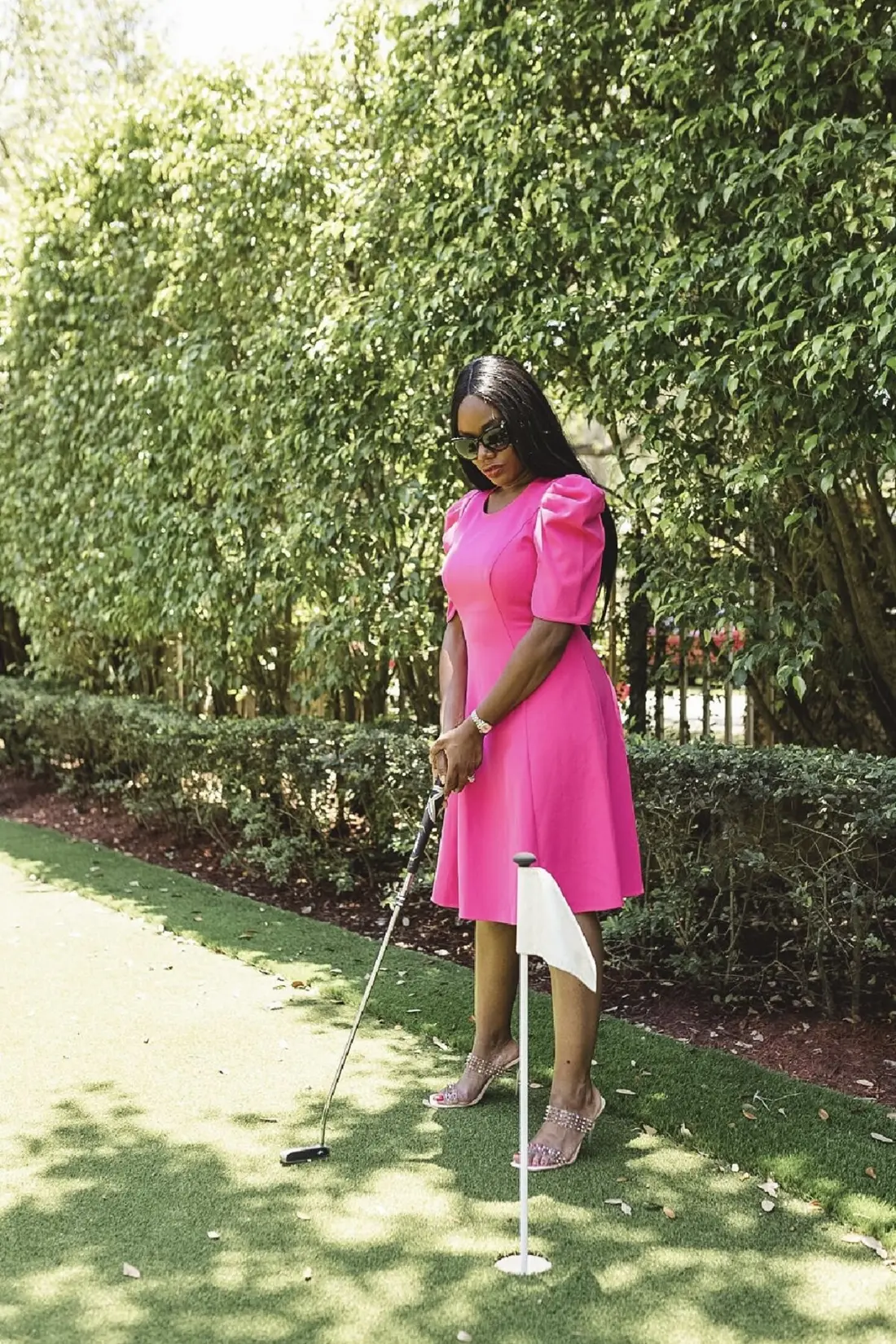 Sharonda in a pink dress lining up a putt on a green