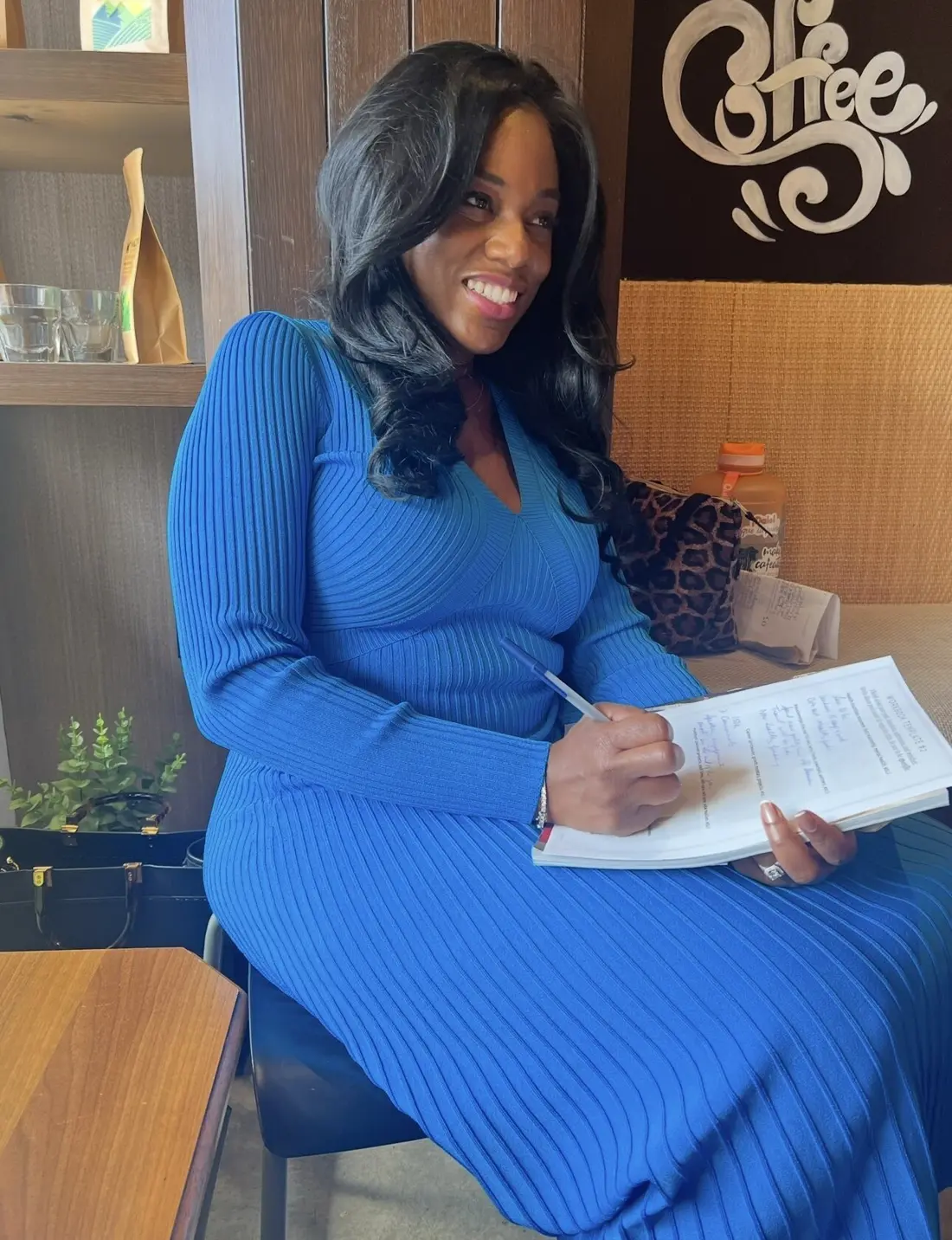 Sharonda in a blue knit dress writing in a notebook