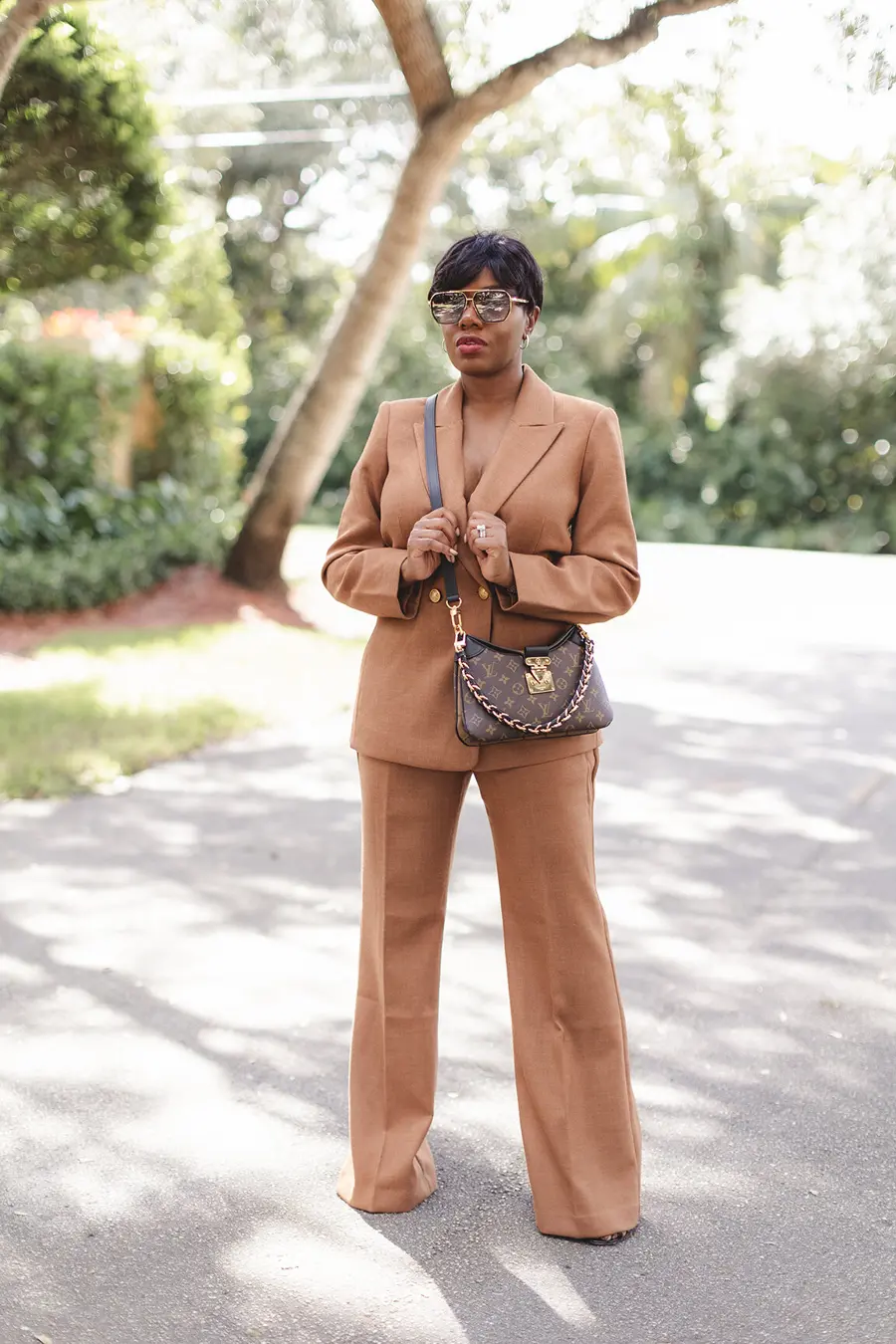 Sharonda in a camel trouser suit with sunglasses and a shoulder bag